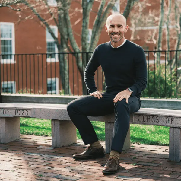 Economics professor sits on a curved concrete bench engraved with &quot;Class of 1923.&quot;